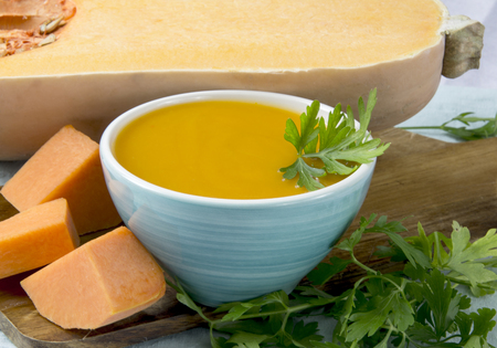 Pumpkin soup served in a bowl, on a table with ingredientsの写真素材