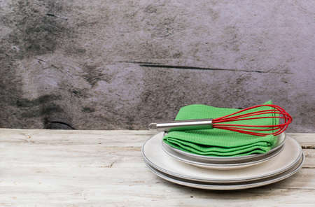 Plates with kitchen towels and cooking utensils on a wooden table with a gray background