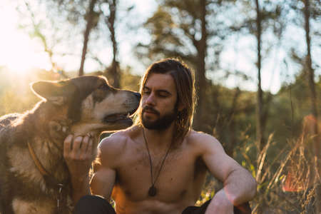 Portrait of a bearded man with his old dog and a beautiful sunset on the mountainの写真素材