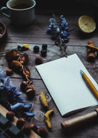 Blank paper with a yellow pencil in a wood table with dates, cinnamon, lemon, turmeric dry root, blue flowers, blueberries, moody.の写真素材