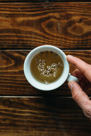 white cup of tea with one hand on a wooden tableの写真素材