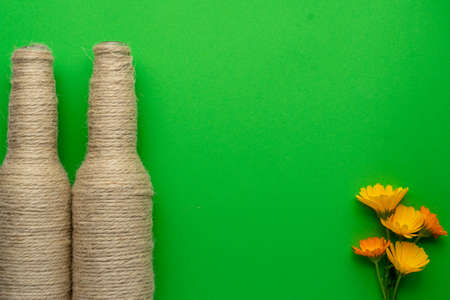 Two glass bottles of beer reused with hemp yarn and flowers on the left with a green background. Recycling and reusable conceptの写真素材