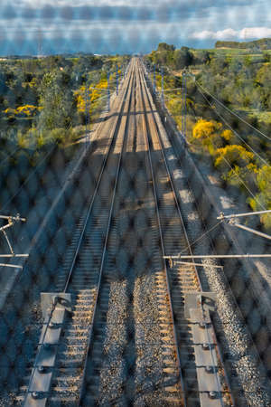 Train tracks located between the mountains, seen from the bridge through the gate. Depth and path concept.の写真素材