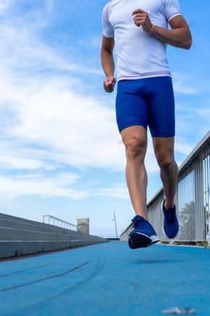 Young runner man in blue pants and white t-shirt running in the sun on a blue track. Motivation...