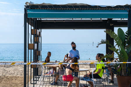 BARCELONA, SPAIN - MAY 25th 2020: First day of the phase 1 of the coronavirus disease (COVID-19) in Barcelona, first day the terraces open at 50% of their capacity, a waiter with a mask attends to a couple on a rather empty terraceのeditorial素材