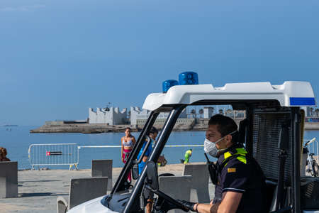 BARCELONA, SPAIN - MAY 25th 2020: First day of the phase 1 of the coronavirus disease (COVID-19) in Barcelona, policeman with a mask driving an electric light urban vehicle near the beachのeditorial素材