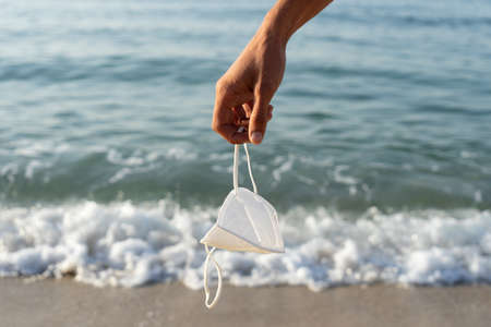 Used covid-19 coronavirus mask caught by hand on the seashore. Responsibility, contagion, cleaning and garbage concept.の写真素材
