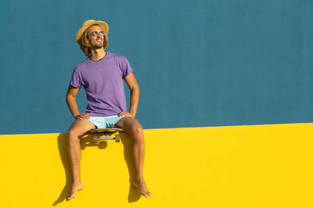 Blond young man with skateboard, hat and sunglasses enjoying the summerの写真素材