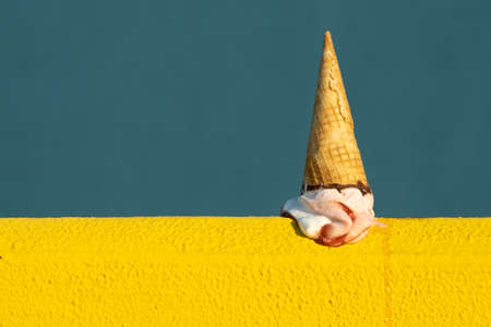 Ice cream with a cone melting in summer with the heat of the sun on a yellow and blue background....