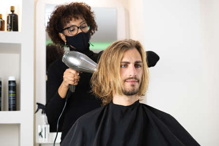 Handsome blonde male client getting haircut by black female hairdresserの写真素材