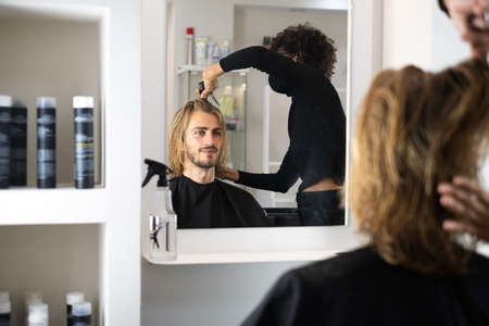 Handsome blonde male client getting haircut by black female hairdresserの写真素材