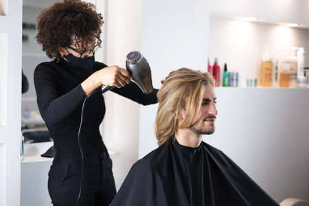 Handsome blonde male client getting haircut by black female hairdresser