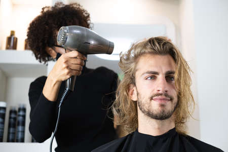 Handsome blonde male client getting haircut by black female hairdresserの写真素材