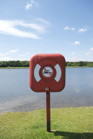 A royalty free stock image of a life belt in case displaying a no swimming symbol against a lake and clear blue sky providing copy space aboveの写真素材