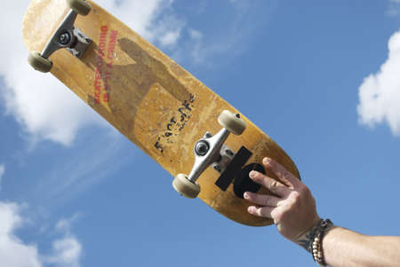 A royalty free stock image of a skateboarder holding their skateboard in the air against sky with the words skateboarding is not a crime on the underside of the boardの写真素材