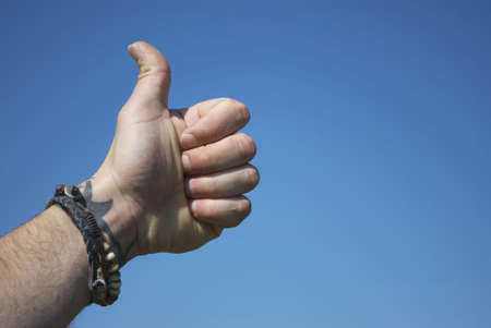 Royalty free stock image of a males hand, thumb raised, wearing surf beads around wrist with tattoo with copy space to the rightの写真素材