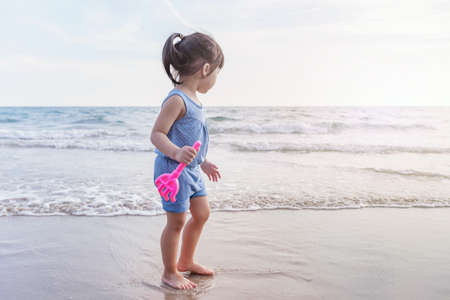 little asian adorable girl 2-3 years plays joyfully on the beach in sunsetの写真素材