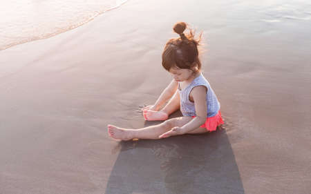 little asian girl 2-3 years sit and plays on the beach in summer time sunsetの写真素材