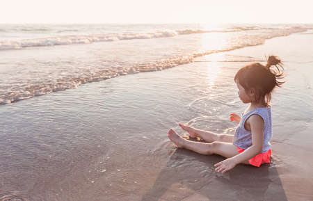 little asian girl 2-3 years sit and plays on the beach in summer time sunsetの写真素材