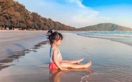 little asian girl 2-3 years sit and plays on the beach in summer time sunsetの写真素材