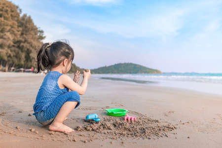 little asian girl 2-3 years sit and plays with imagination on the beach in summer time sunsetの写真素材