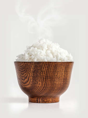cooked jasmine rice in wooden bowl with steam on white backgroundの写真素材