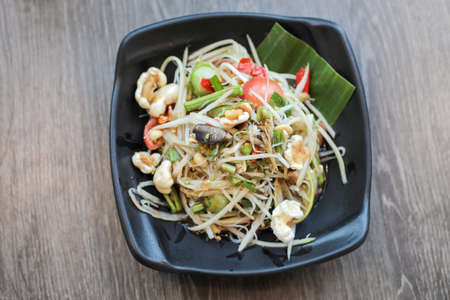 Papaya salad, Thai traditional food or name in Thai Somtum, papaya in fermented fish sauce with vegetable and pork cracklings in black dish on wooden tableの写真素材