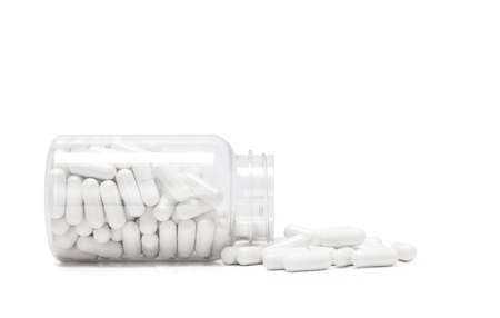 white medicine capsules spill out from transparent bottle and isolated on white background