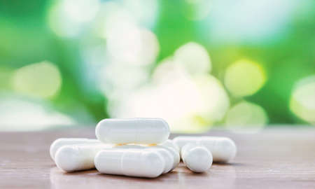 white medicine capsule in selective focus on top wooden table with green natural bokeh backgroundの写真素材