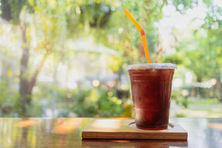 ice black coffee or americano in plastic cup with orange straw on wooden table and greenery garden background in the morning refreshing sunriseの写真素材