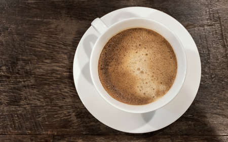 top view of black hot coffee and bubbles detail in white cup on vintage wooden top table with copy...