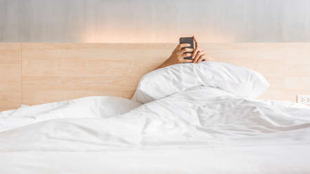 Man waking up and use smartphone or mobile phone on the bed in white blanket at morning time, social lifestyle conceptの写真素材