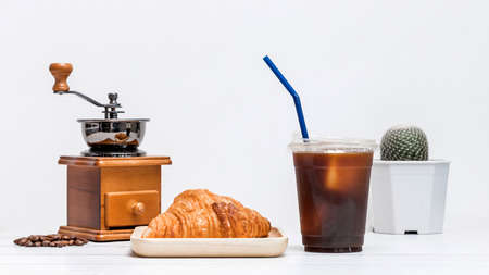 ice americano coffee in a cup with croissant on wooden plate and coffee bean grinder ready for breakfast mealの写真素材