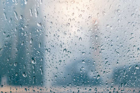 Raindrops over the window with buildings of the city in the background on a rainy dayの写真素材