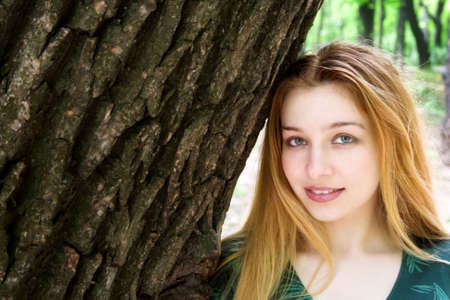 Beautiful blond girl standing along big treeの写真素材