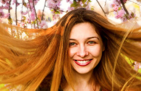 Happy woman with beautiful long hair and flowers in backgroundの写真素材