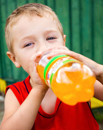 Thirsty child drinking unhealthy bottled orange sodaの写真素材