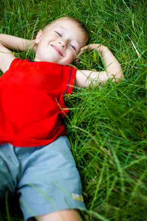 Happy joyful boy relaxing on green fresh grassの写真素材