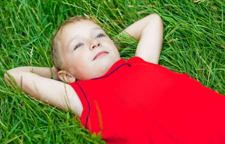 Pensive kid day dreaming in fresh grassの写真素材