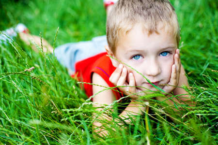 Cute blond boy relaxing on green fresh grassの写真素材