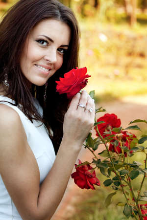 Happy young woman in flower garden smelling red rosesの写真素材