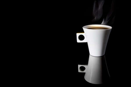 A cup of steaming coffee on a reflecting surfaceの写真素材