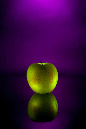 A green apple on a reflective surface with a purple backgroundの写真素材