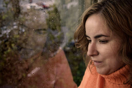 Portrait of a young woman looking through the window on a rainy day in autumnの写真素材