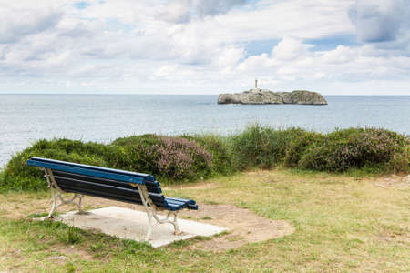 An empty bench looking at a lighthouse in the Mouro Island, Santander  Spain の写真素材