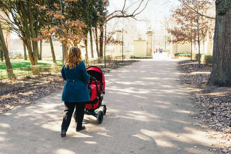 Mother walking with baby stroller in parkの写真素材