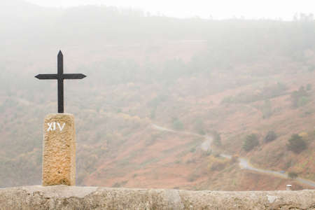 Cross with a road in a forest in the background during a misty dayのeditorial素材