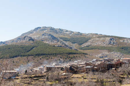Smoking chimneys in the village of Valverde de los Arroyos, one of the Black Villages Guadalajara (Spain), with the Ocejon Peak in the backgroundの写真素材