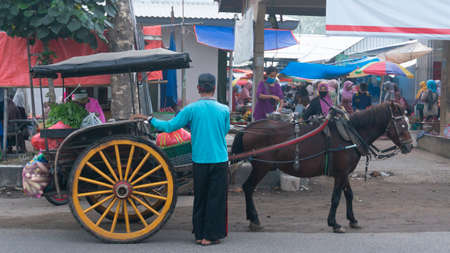 A horse cart driver is waiting for a passenger in a traditional market. horse-drawn buggy is a traditional transportation that is still used by rural communities. Ponorogo, Indonesia- 10/05/2020のeditorial素材