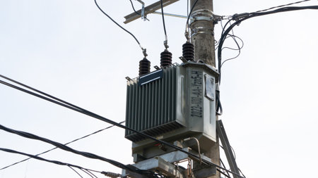 A detailed shot of an electrical transformer mounted on a concrete utility pole, surrounded by a complex network of power lines against a clear sky.の写真素材